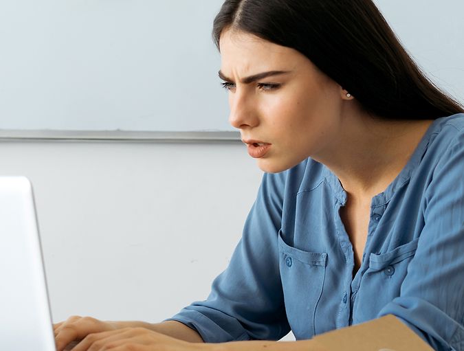 Donna che aggrotta la fronte e strizza gli occhi guardando il suo laptop