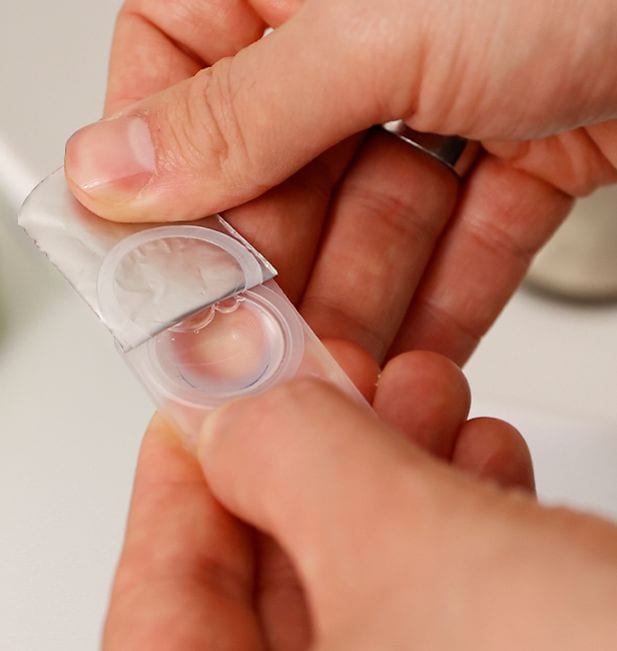 Primo piano di mani che aprono blister di lente a contatto in bagno