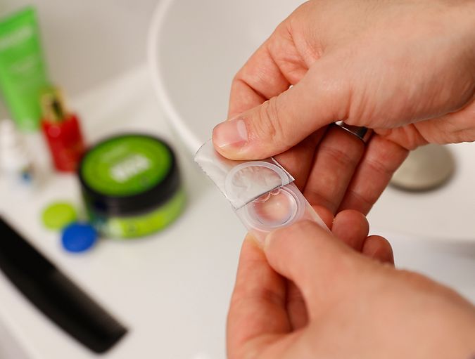 Primo piano di mani che aprono blister di lente a contatto in bagno